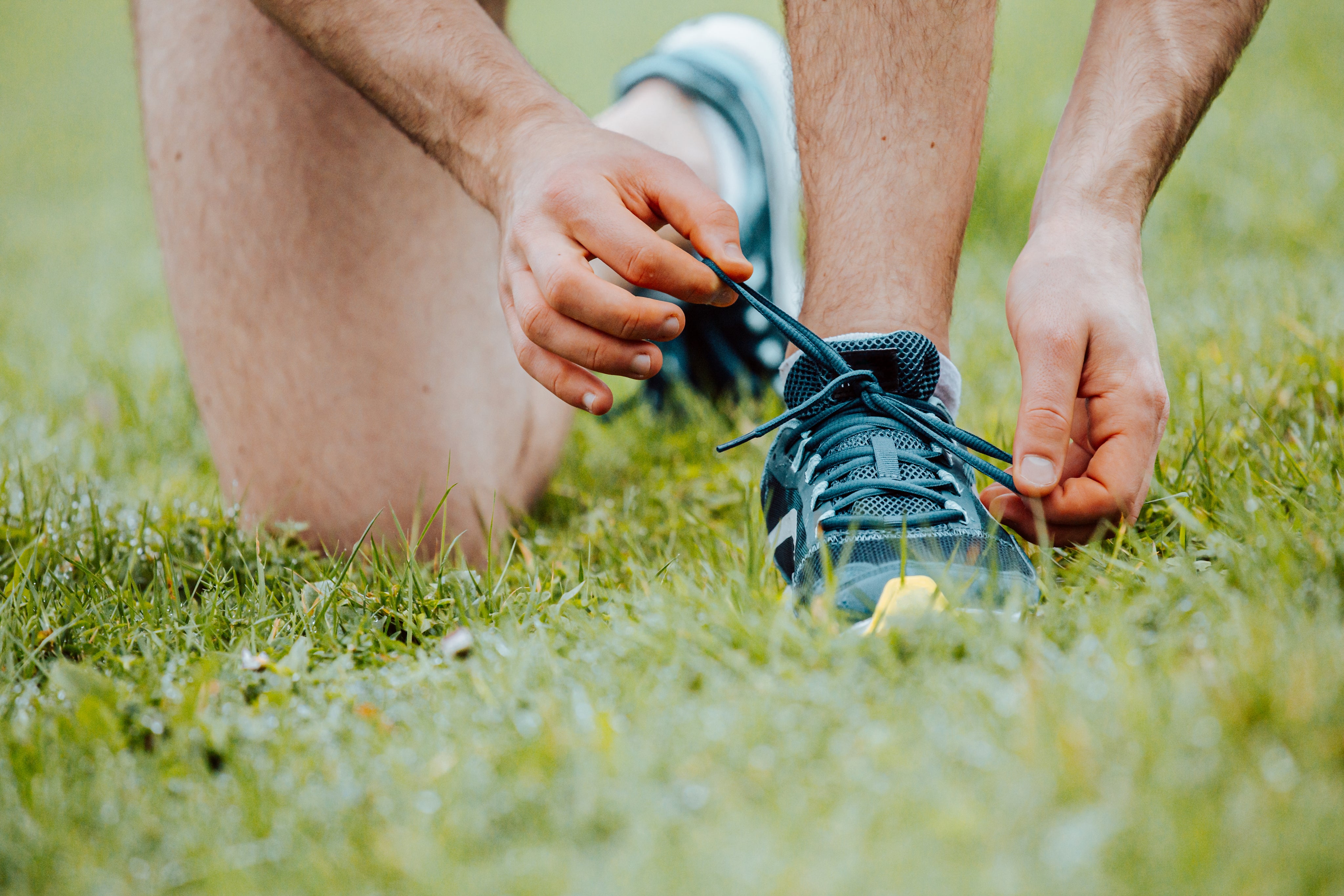 person-kneels-on-grass-to-tie-their-shoelaces.jpg